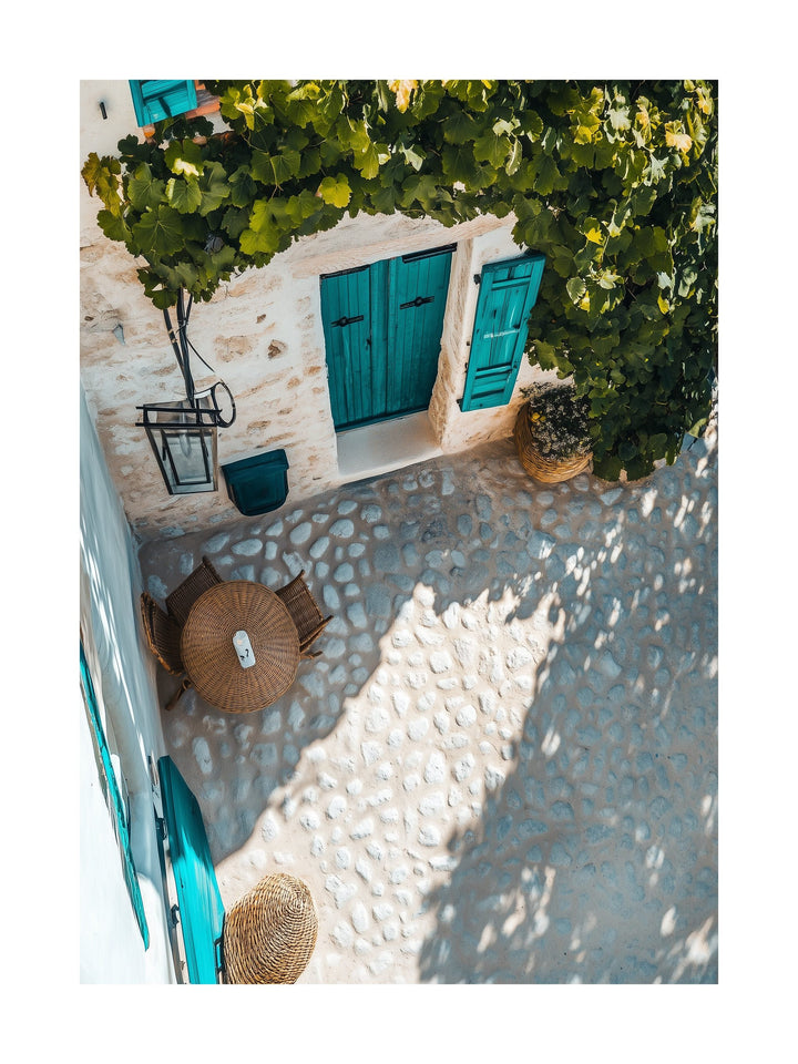 Overhead view of a Mediterranean courtyard with blue doors, vine shade, and stone pavement. Ideal for wall art in your home, office, or studio.