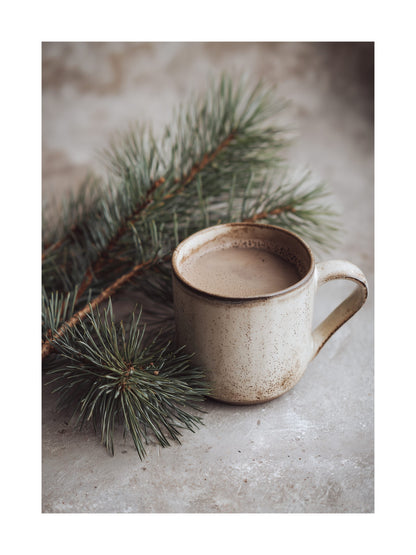 Ceramic mug of hot cocoa placed beside pine branches on a textured surface.
