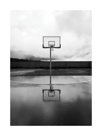 Black and white photo of basketball hoop and reflection on wet court