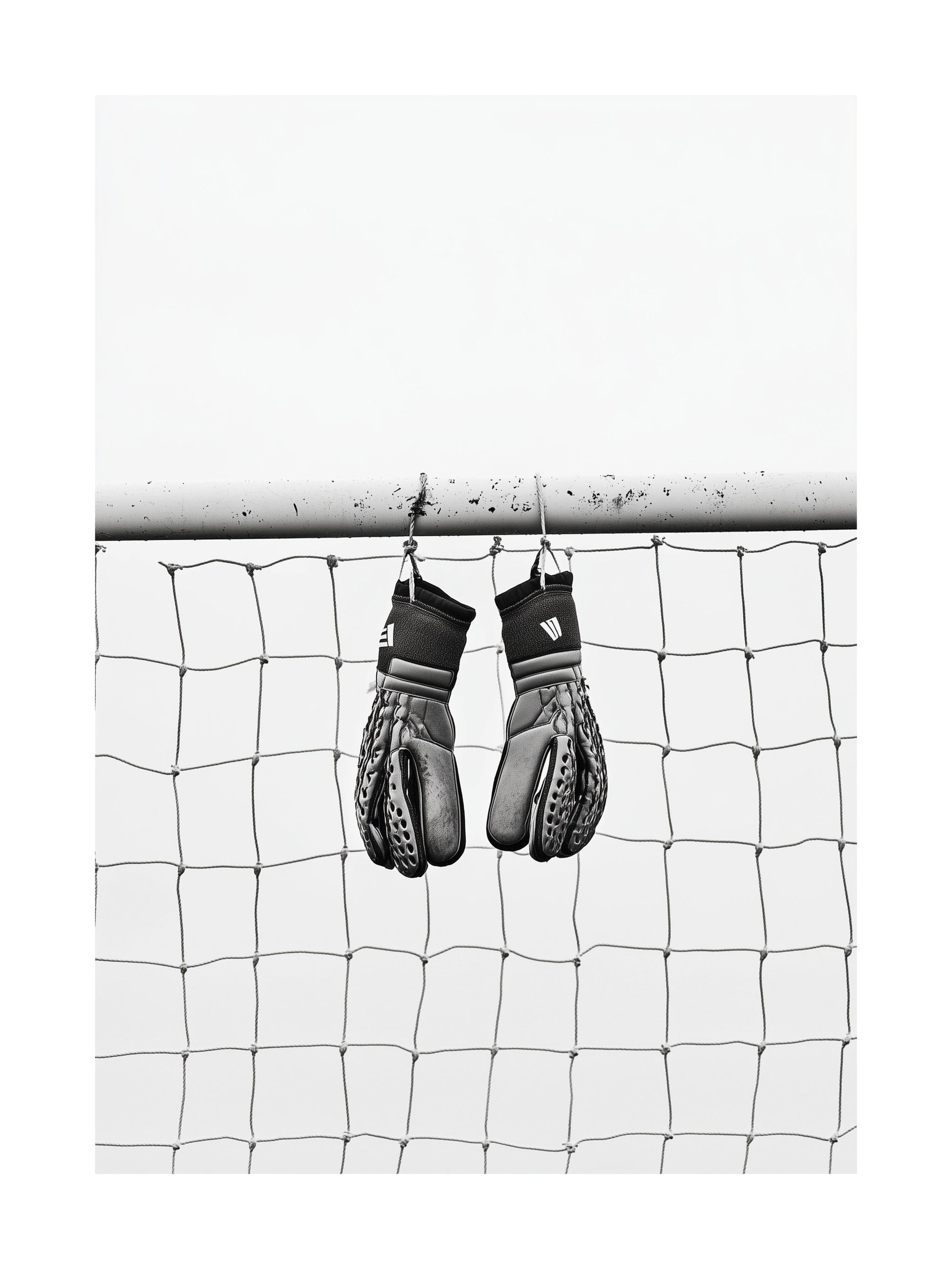 Black and white image of goalkeeper gloves hanging on goalpost