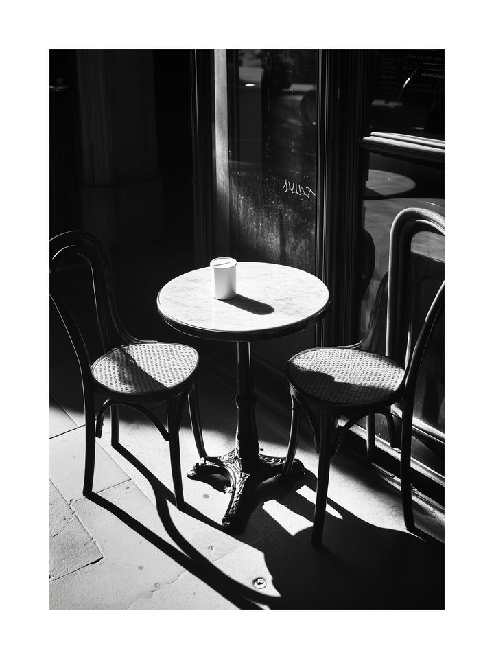 Black and white photo of a sunlit café table with two chairs